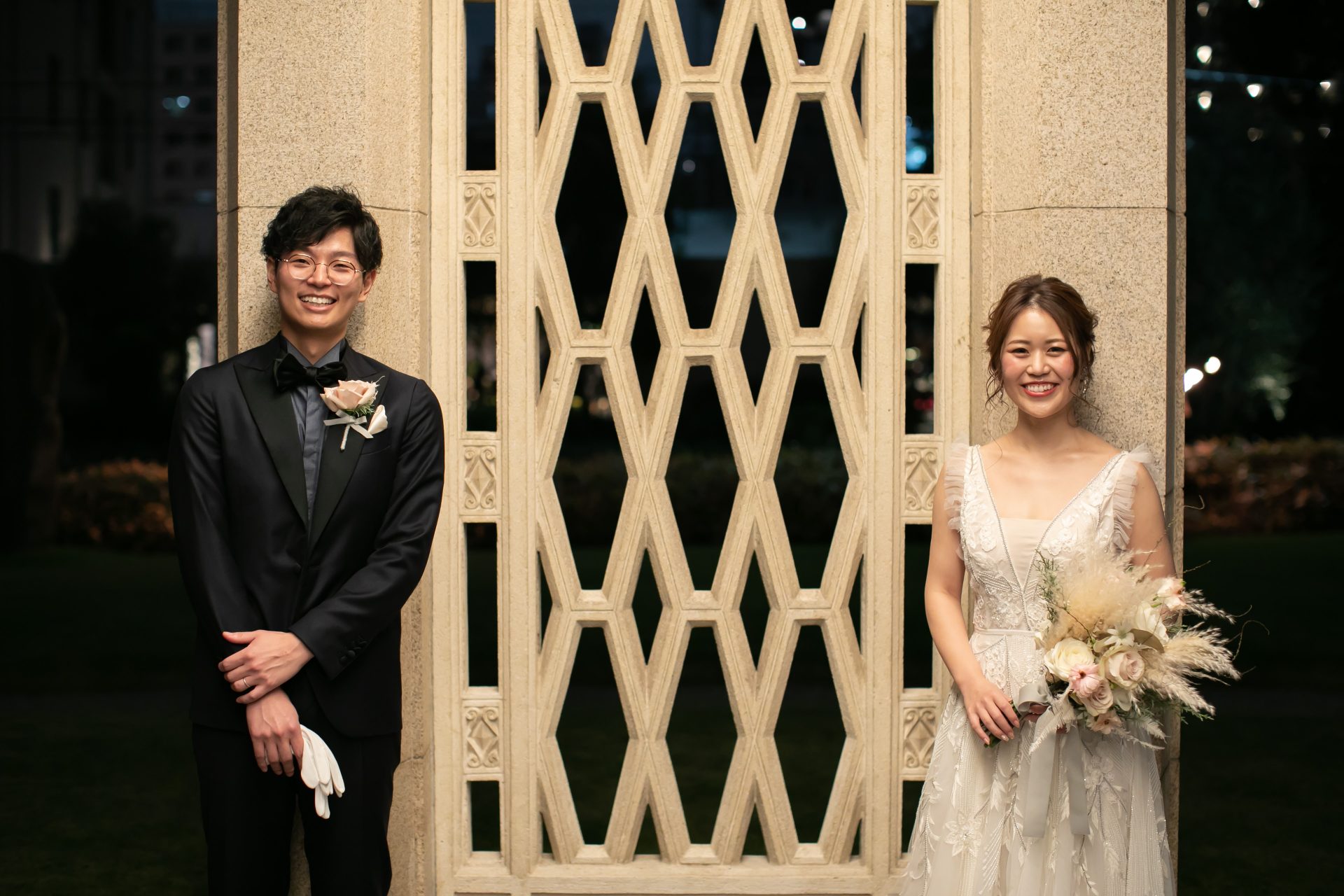 ザ・ガーデンオリエンタル大阪のエントランスにあるレリーフテラコッタの外壁の前で笑顔を見せられるご新郎ご新婦様