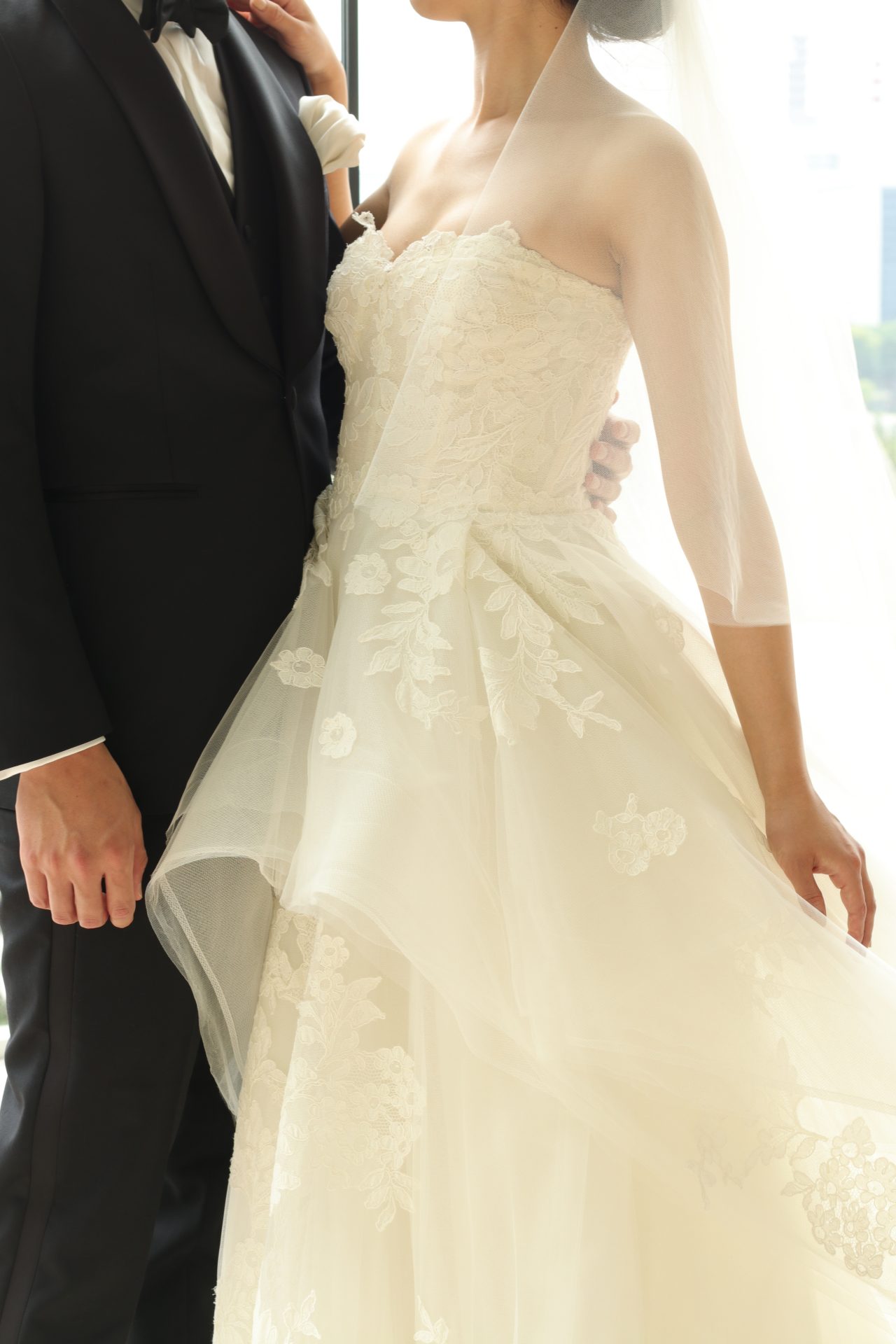 女性のお身体を綺麗に見せるためにデザインされたレースが施されたペプラムスカートのウェディングドレスに、フォーマルなブラックタキシードの組み合わせで、上品でスタイリッシュな大人のホテルウェディングスタイルの完成です