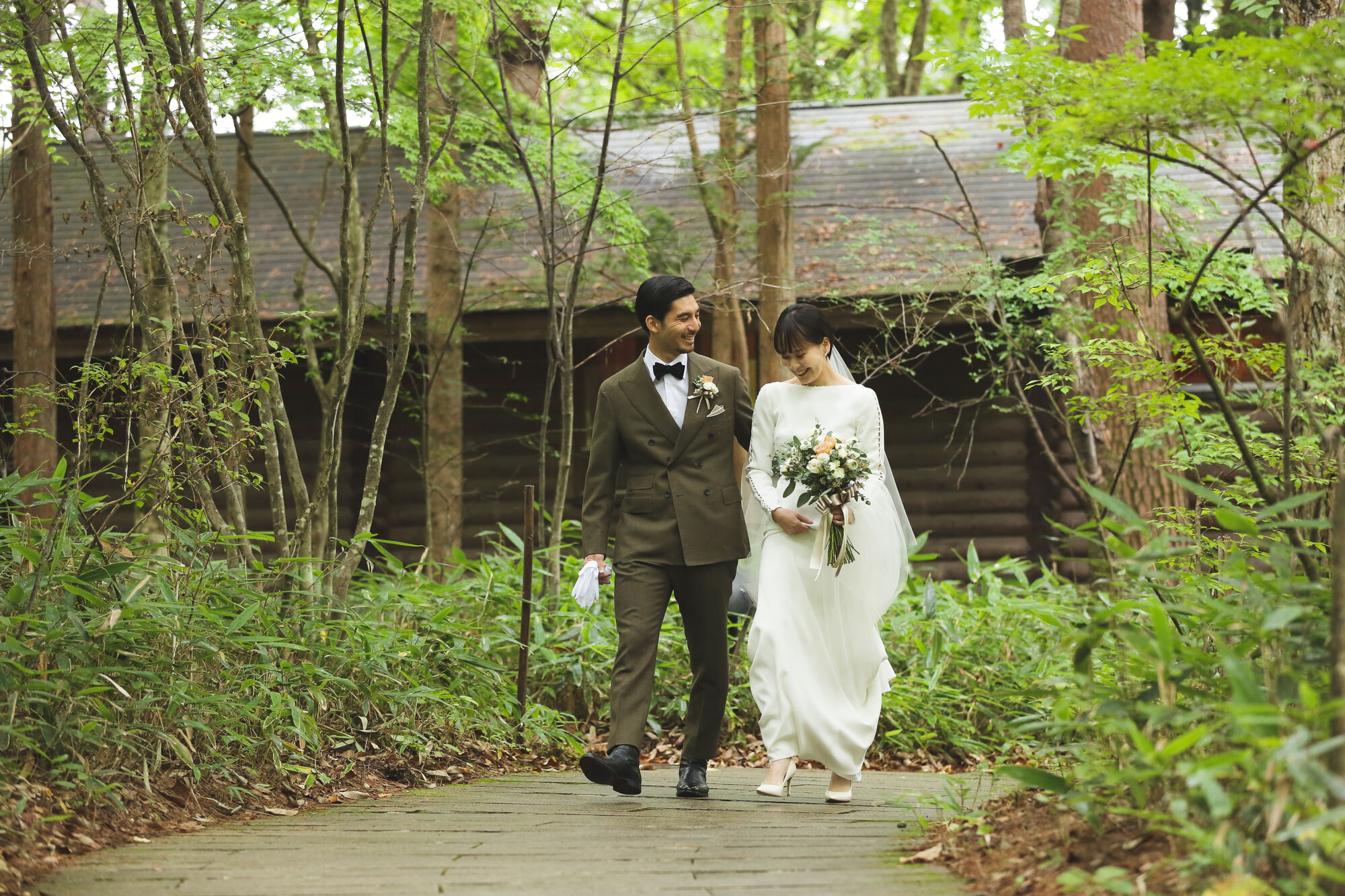 リゾートウェディングを軽井沢高原教会で叶えたお二人がトリートドレッシングのドレスを着て歩いている様子。