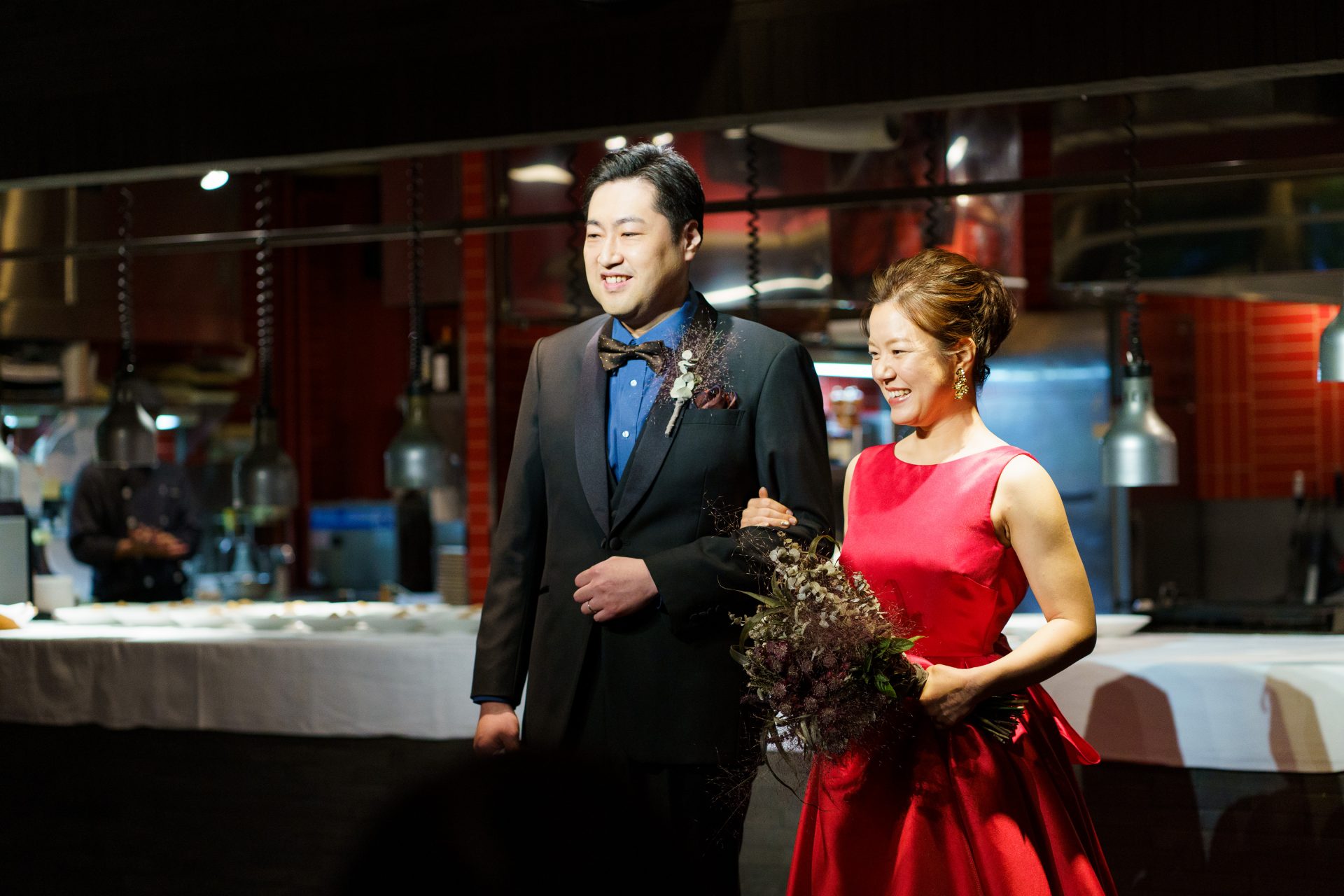 シックなバンケットの雰囲気に映えるTHE TREAT DRESSINGの赤いサテンのウェディングドレスをお召しになったご新婦様