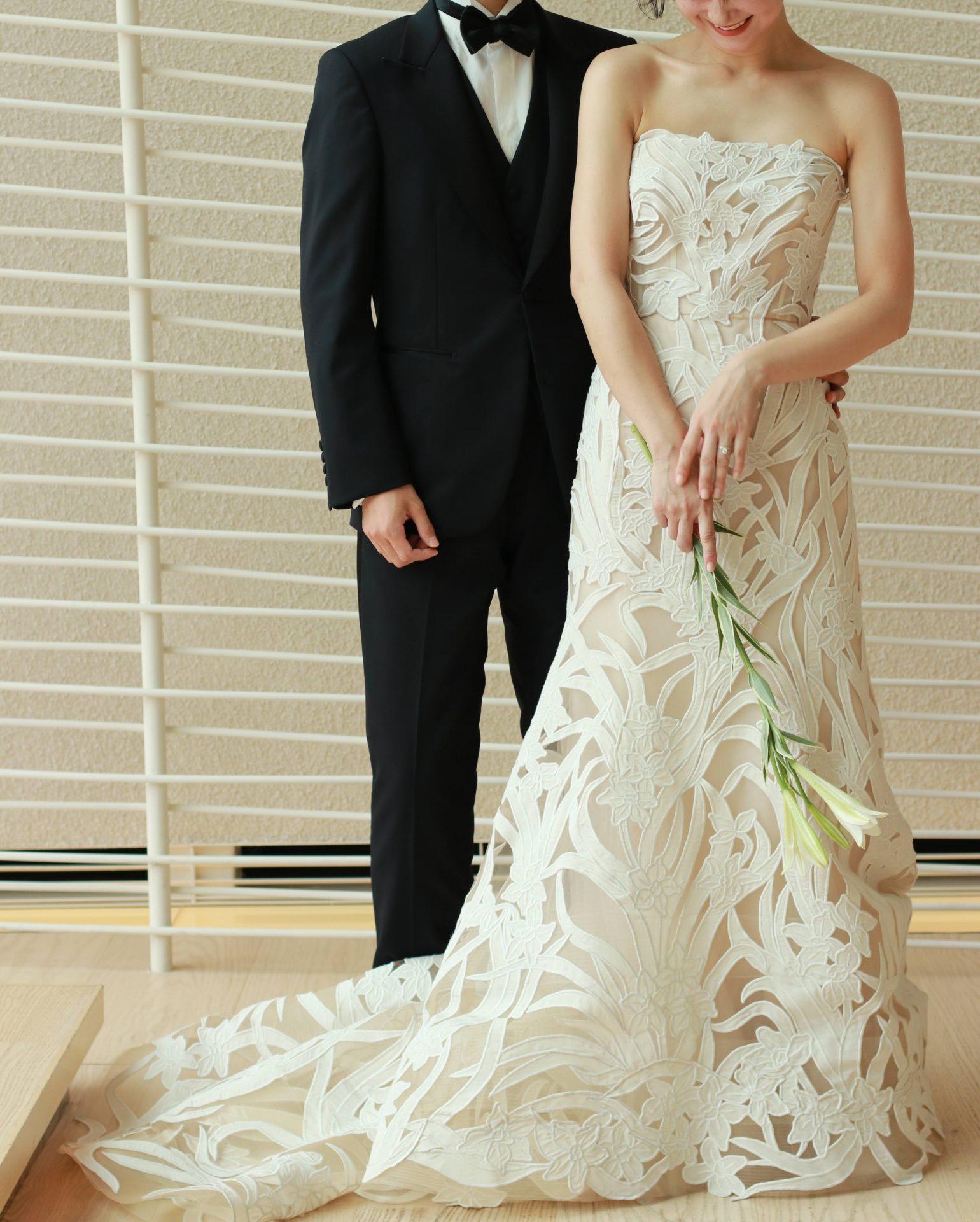 結婚式当日の新郎新婦が横に並んだ時、シンプルなブラックのタキシードと華やかな総レースのウェディングドレスがお互いを引き立てあいます