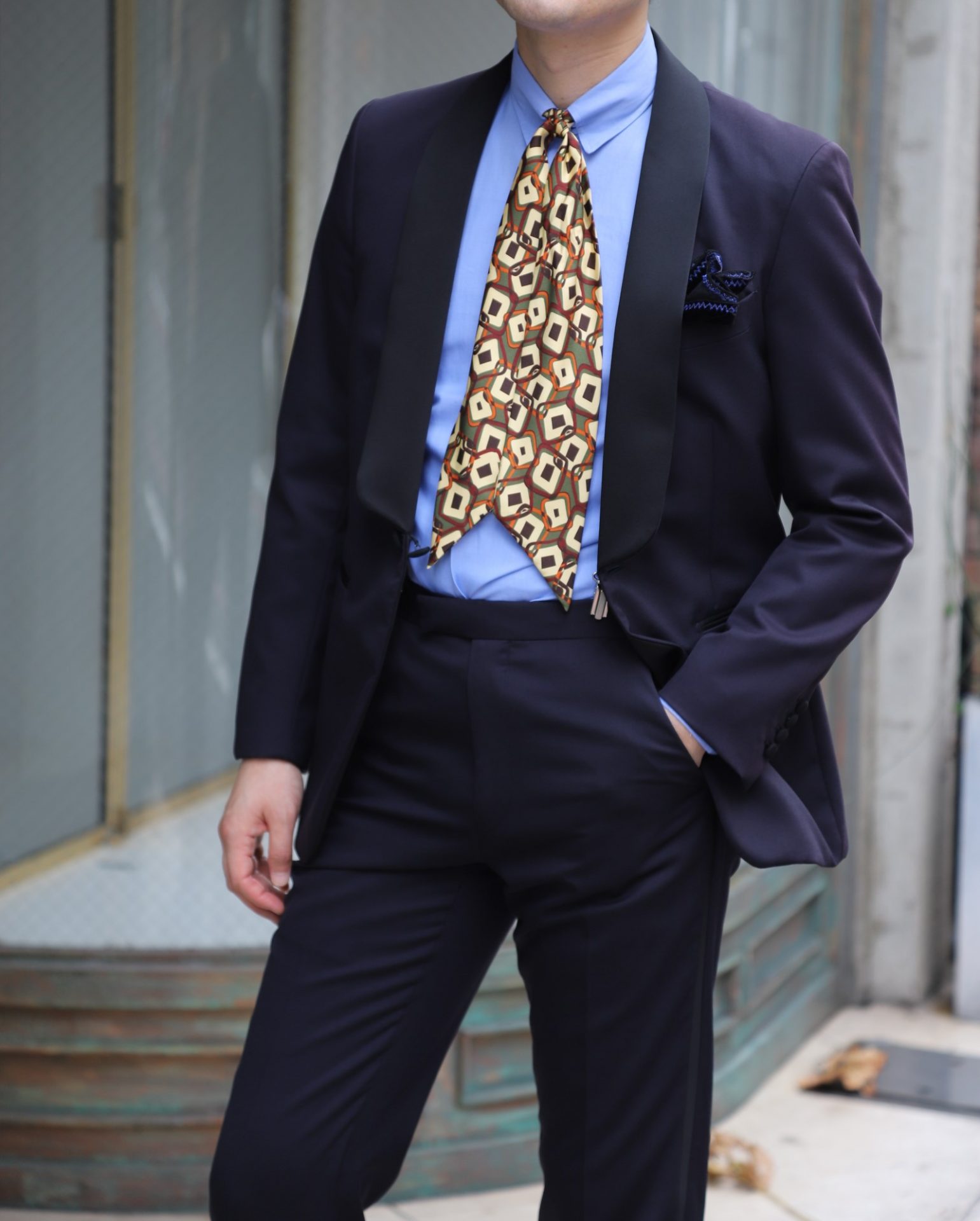 正統なミッドナイトブルーのタキシードに身を包み、タブカラーシャツの色目はサックスブルーをチョイスしクラシカルとモダンの融合を演出。スカーフタイは片結びに巻くことでスマートで垢抜けた印象に仕上げます。