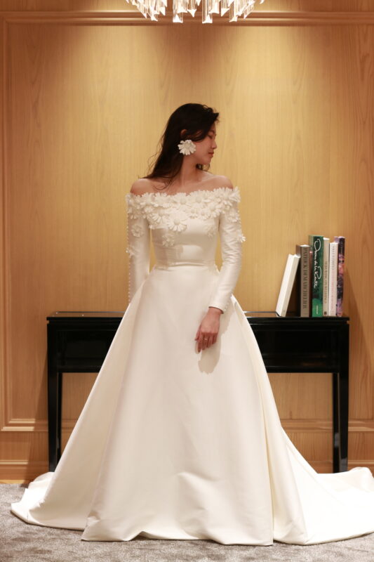 ミカド素材で作られたAラインの美しいシルエットに、デイジーのフラワーモチーフが目を惹くウェディングドレス。ミカドの程よい光沢感とウエストから綺麗に広がるAラインのシルエットは洗練されたエレガンスを演出します。