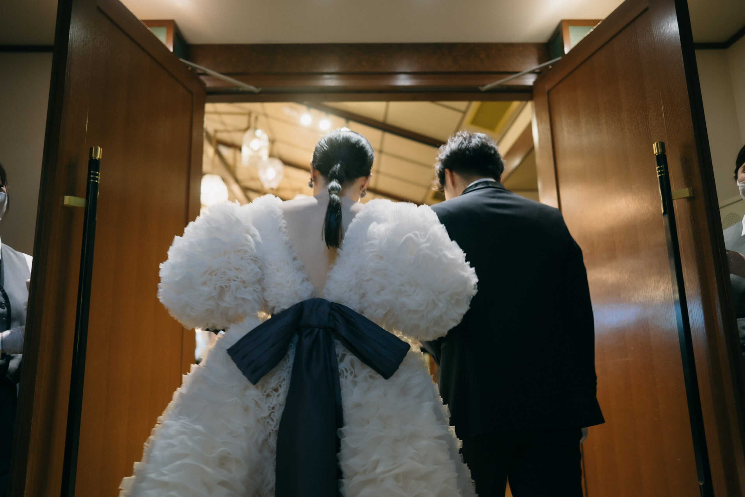 トモコイズミのリボンがバックコンシャスなウェディングドレスでヒガシヤマソウドウの披露宴会場であるパゴダのお部屋にご入場される新郎新婦様