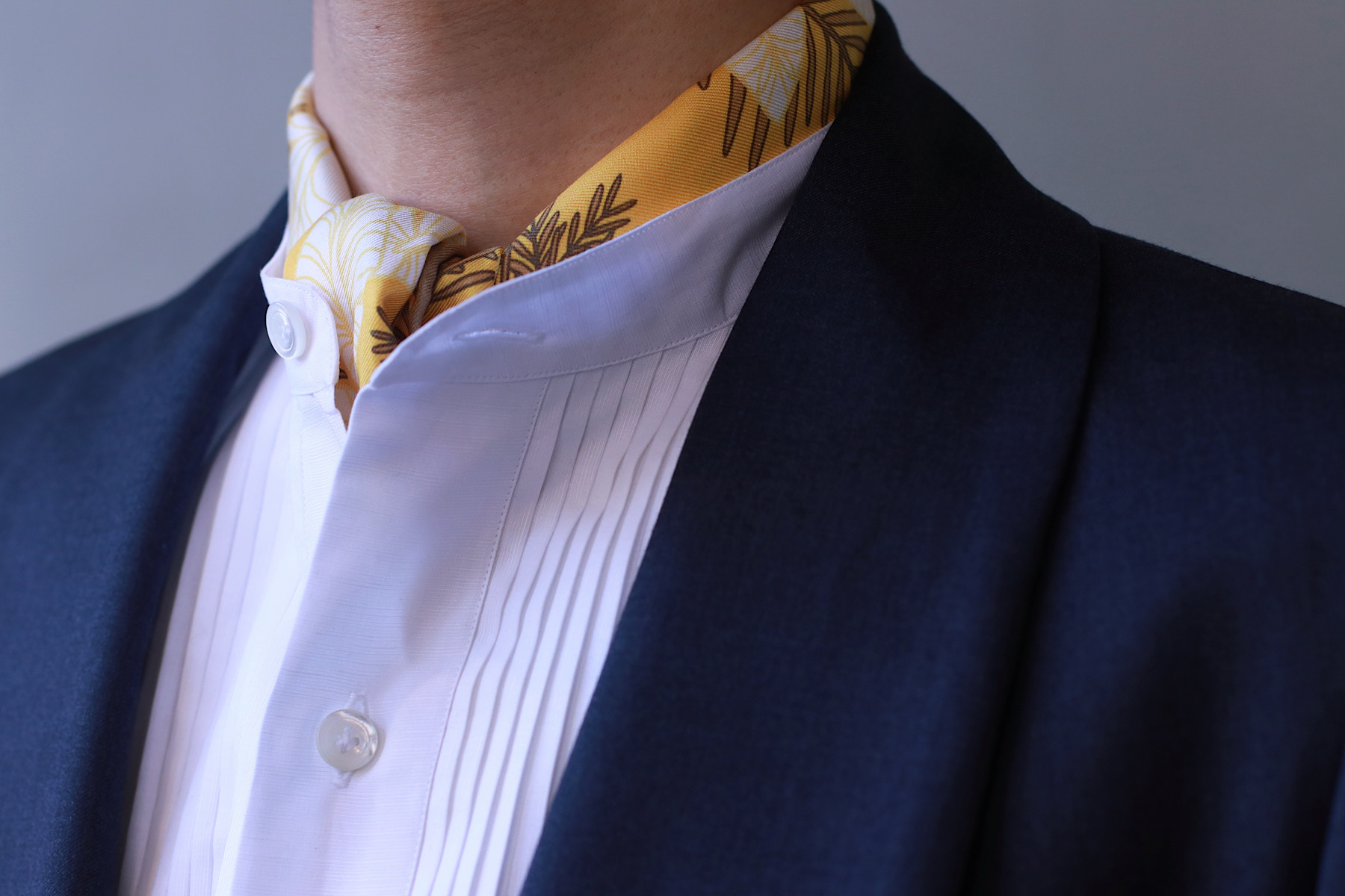 ホワイトのプリーツシャツの首元にはイエローのストールを覗かせてコーディネートにアクセントを