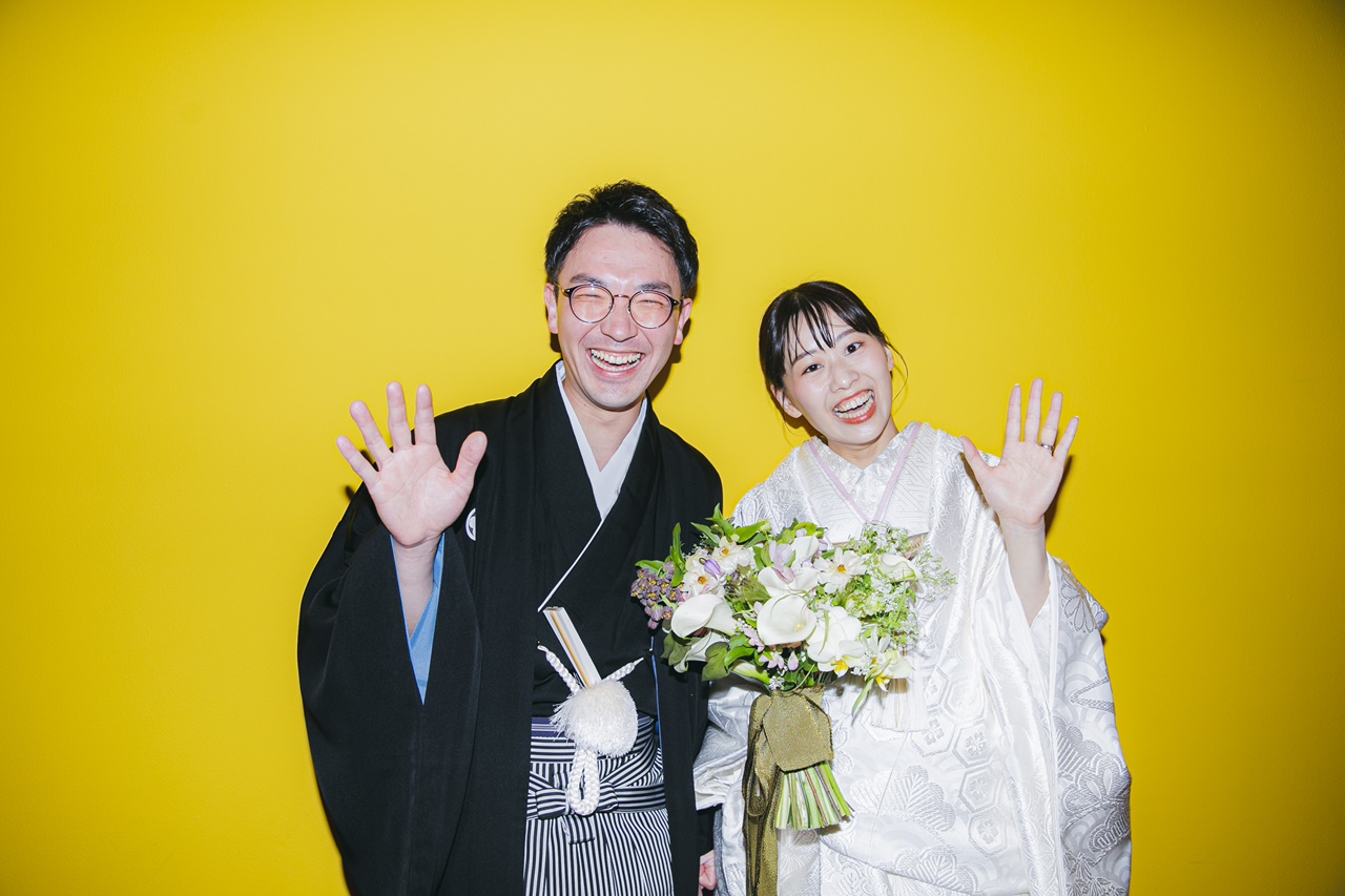 ポップで写真映えする黄色の壁の前での新郎新婦のツーショット