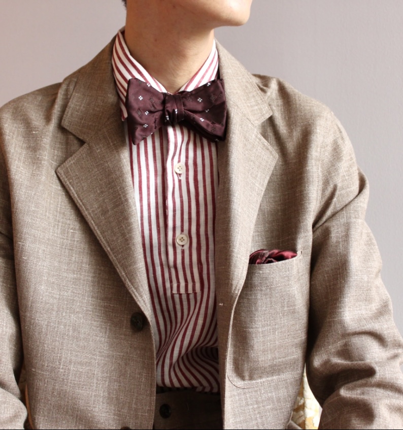 ベージュセットアップに赤ストライプシャツのコーディネートで蝶ネクタイをした結婚式のパーティースタイル