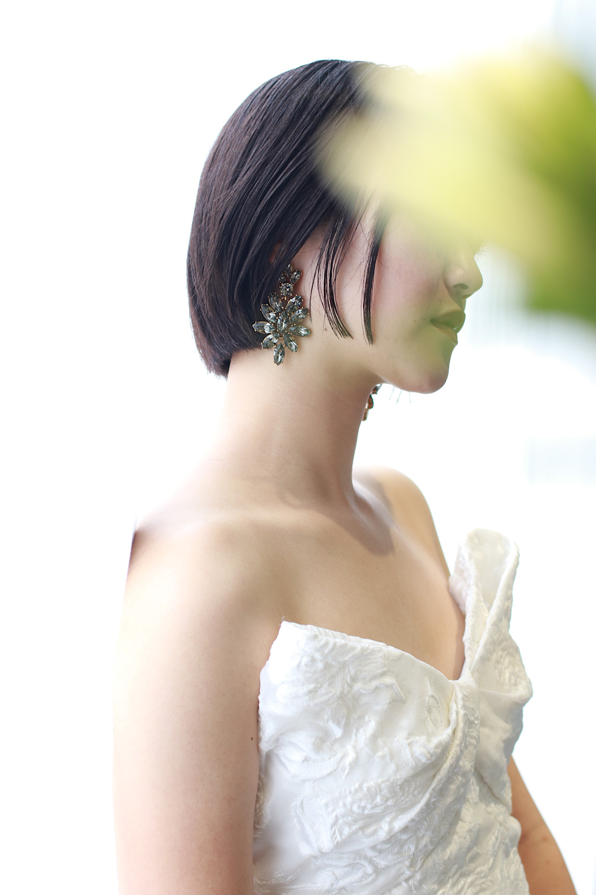 THETREATDRESSINGのモ二ークルイリエの胸元がアイキャッチーなウェディングドレスにモダンなブラックストーンが洗練られたクリーンな印象のコーディネート、白と緑のフラワー越しに映る凛としたミニボブが美しい花嫁姿