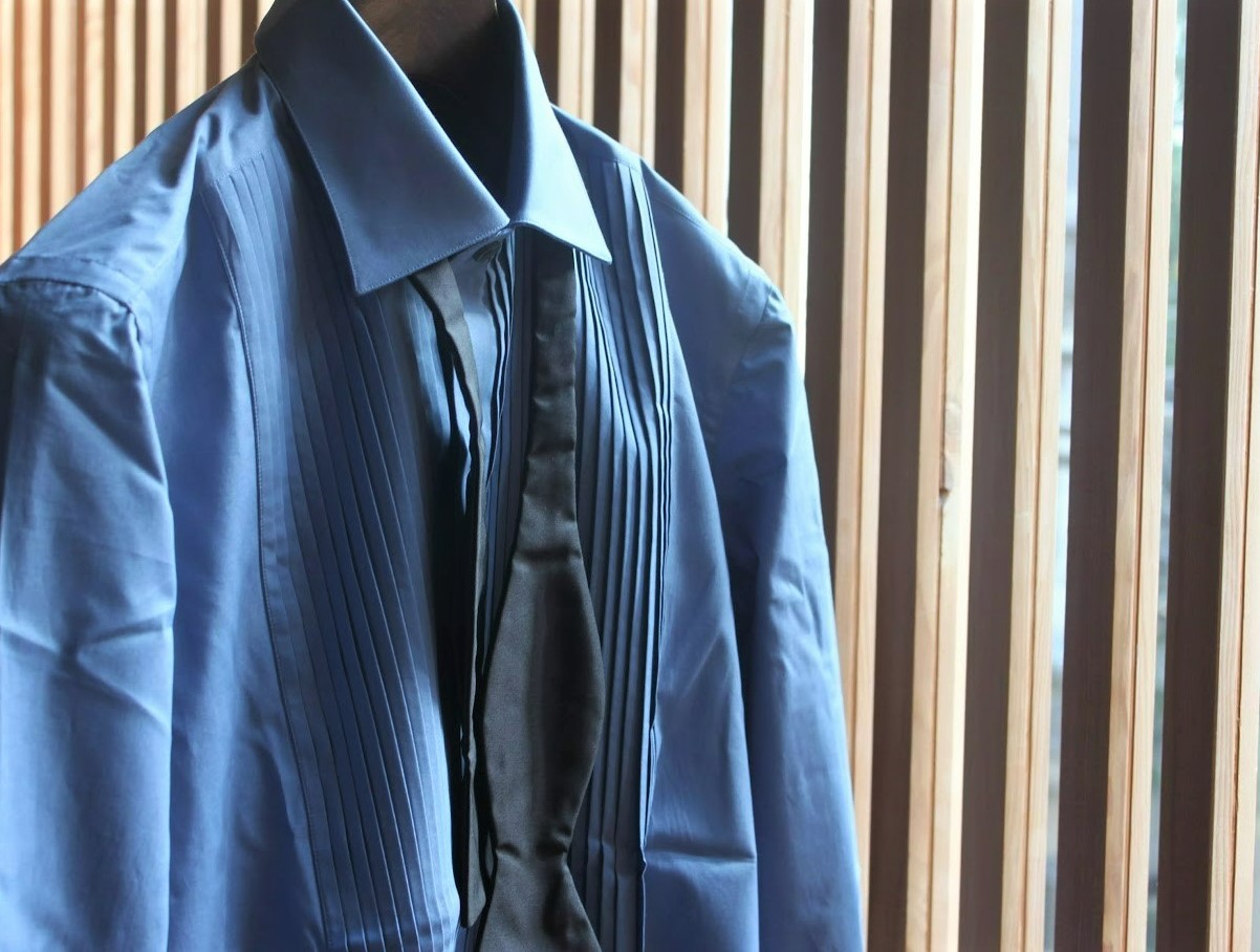 エリコフォルミコラのブルーシャツ。ブラックのボウタイと掛け合わせることでよりドレッシーな印象に。胸元にはプリーツを施したクラシカルなディティールで深みのあるサックスブルー。