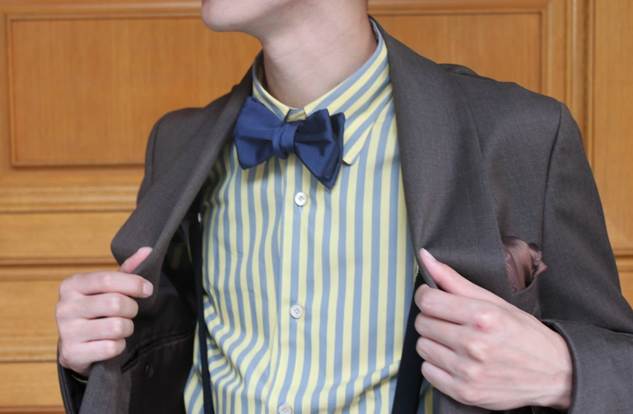 ブラウンタキシードに同じ暖色のイエローストライプシャツのコーディネート。タイはネイビーを使用しアズーロエマローネの配色にすることでそれぞれの小物がより主張し合うようなコーディネート。