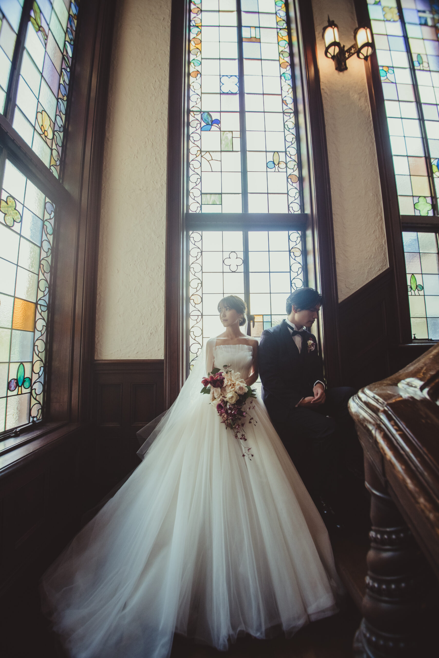 赤坂プリンスクラシックの写真スポットであるステンドグラスの前でAラインチュールの純白のウェディングドレスを見に纏うご新婦様とクラシカルなネイビーのタキシードをお召しになるご新郎様