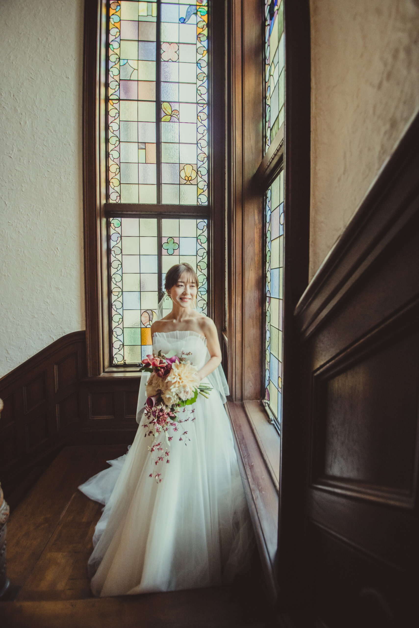 赤坂プリンスクラシックの写真スポットであるステンドグラスの前でAラインチュールの純白のウェディングドレスを見に纏うご新婦様