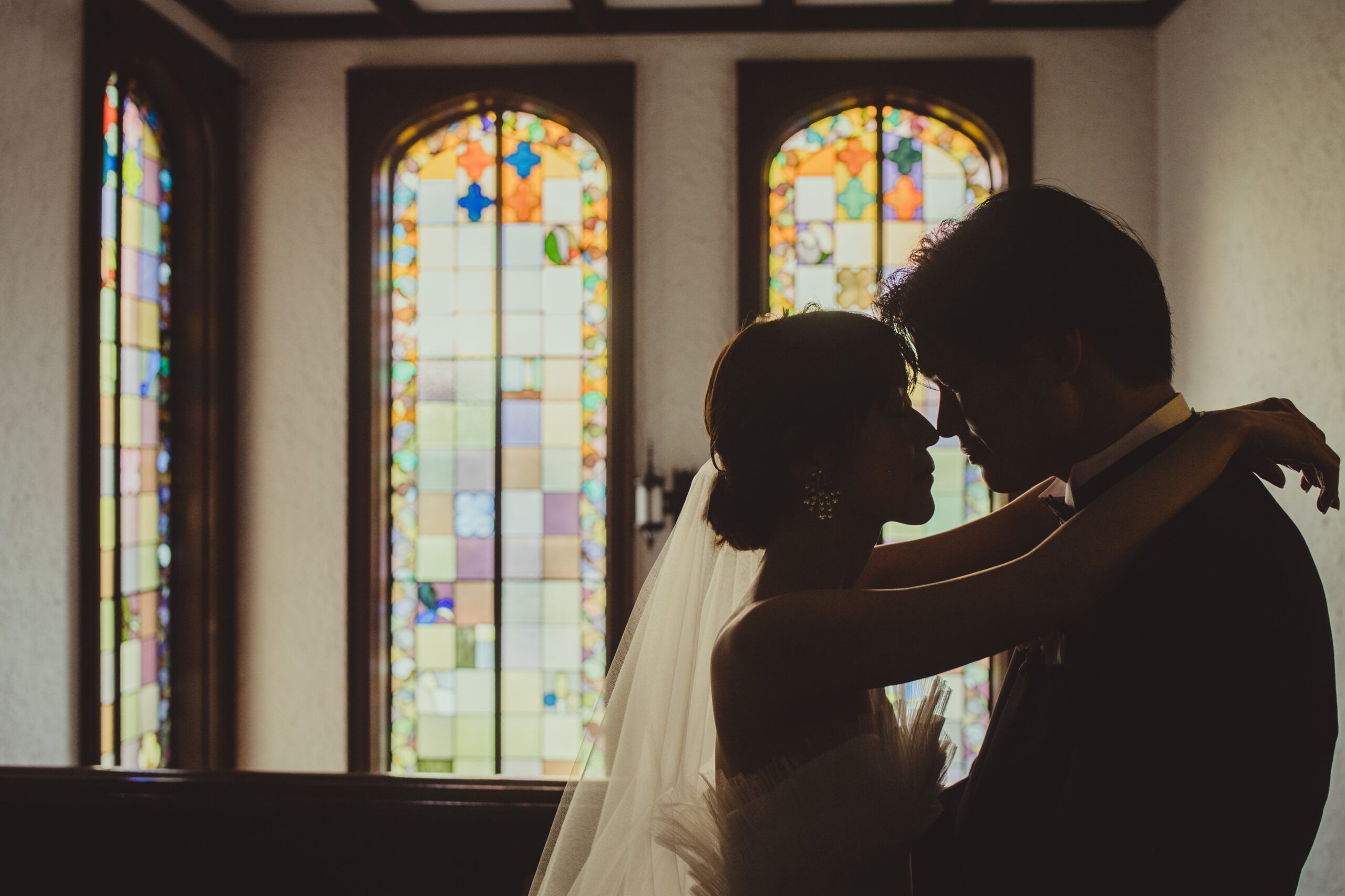 赤坂プリンスクラシックの写真スポットであるステンドグラスの前でAラインチュールの純白のウェディングドレスを見に纏うご新婦様とクラシカルなネイビーのタキシードをお召しになるご新郎様のフォトジェニックな雰囲気