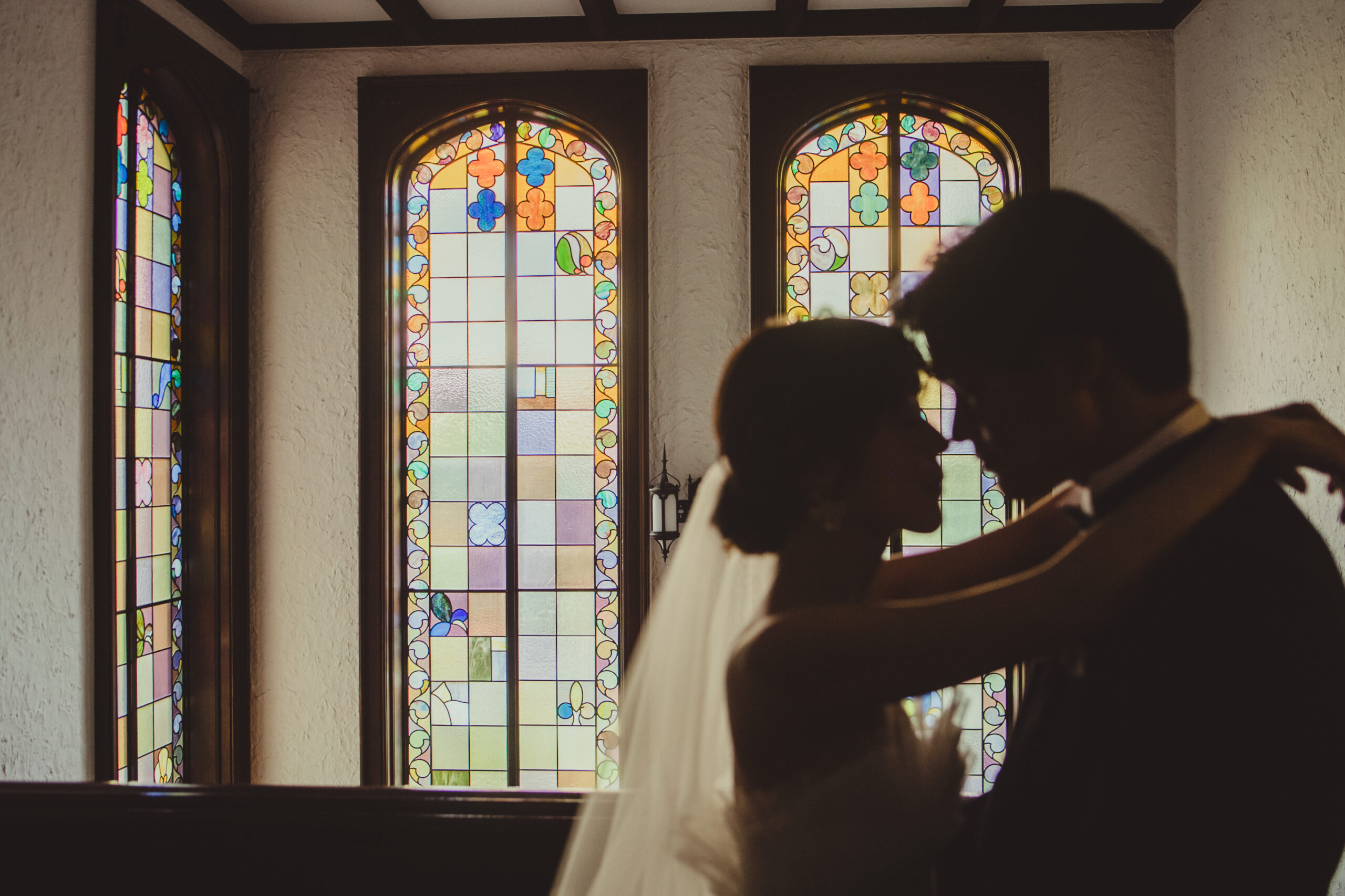 赤坂プリンスクラシックの写真スポットであるステンドグラスの前でAラインチュールの純白のウェディングドレスを見に纏うご新婦様とクラシカルなネイビーのタキシードをお召しになるご新郎様のフォトジェニックな雰囲気