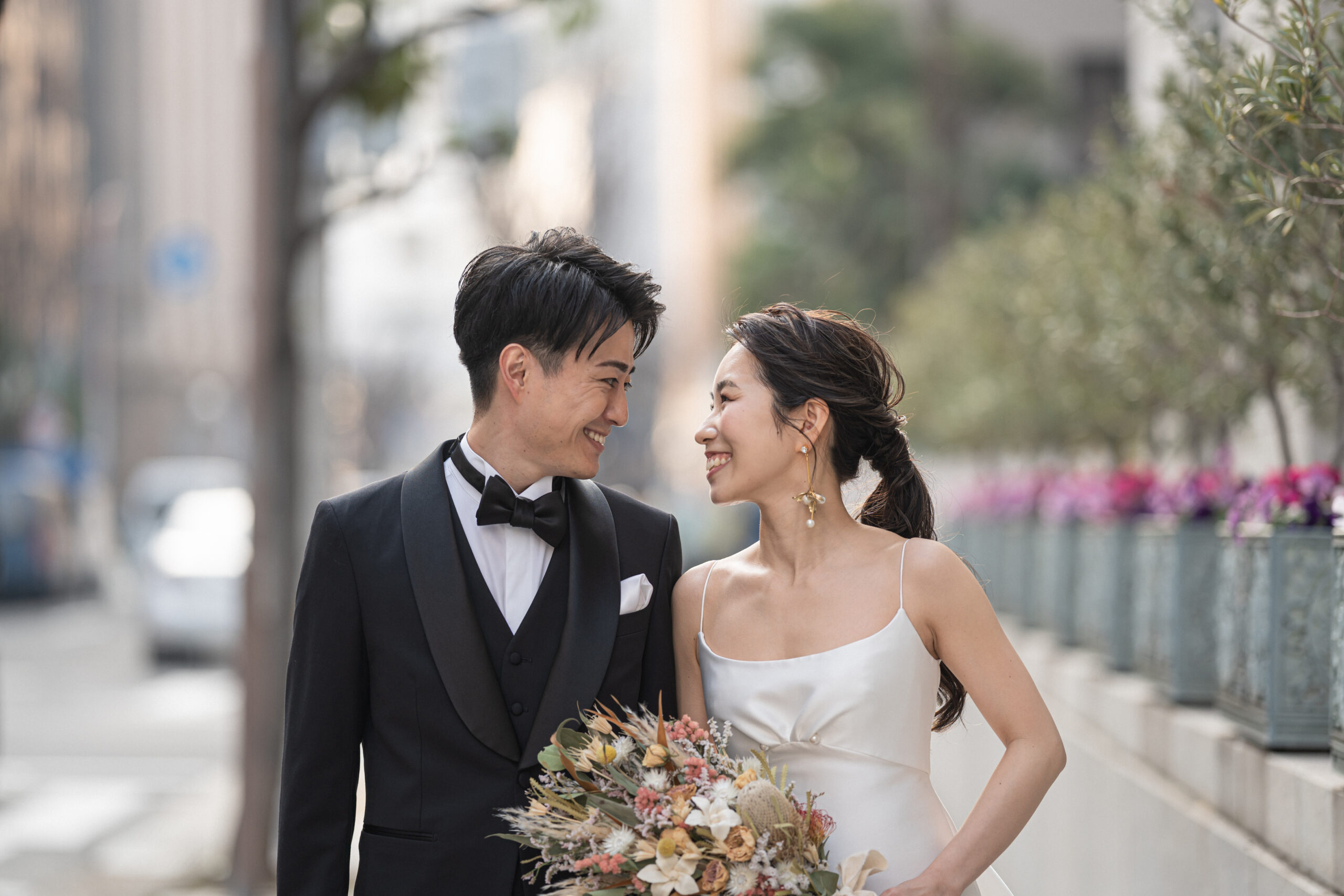 トリートのリラックス感のあるウエディングドレスとブラックタキシードでオリエンタルホテル神戸を背景に居留地の美しい街並みを歩くご新郎様とご新婦様