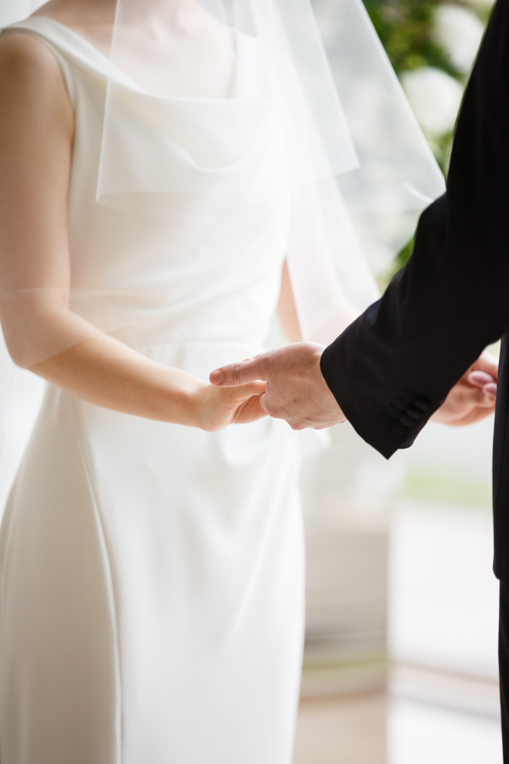 ニューヨーク発の都会的でタイムレスなデザインが特徴のアムサーラのウェディングドレスに身を包むご新婦様と手を取り合い誓いを立てるご新郎様。