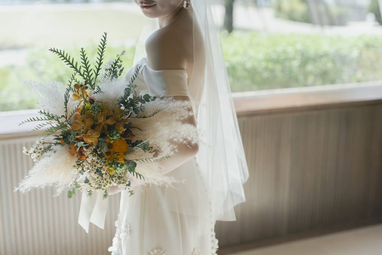 キャッチーなフラワーモチーフのウェディングドレスとイエローを交えたナチュラルなカラーのブーケが新婦様の愛らしさを表現してくれます