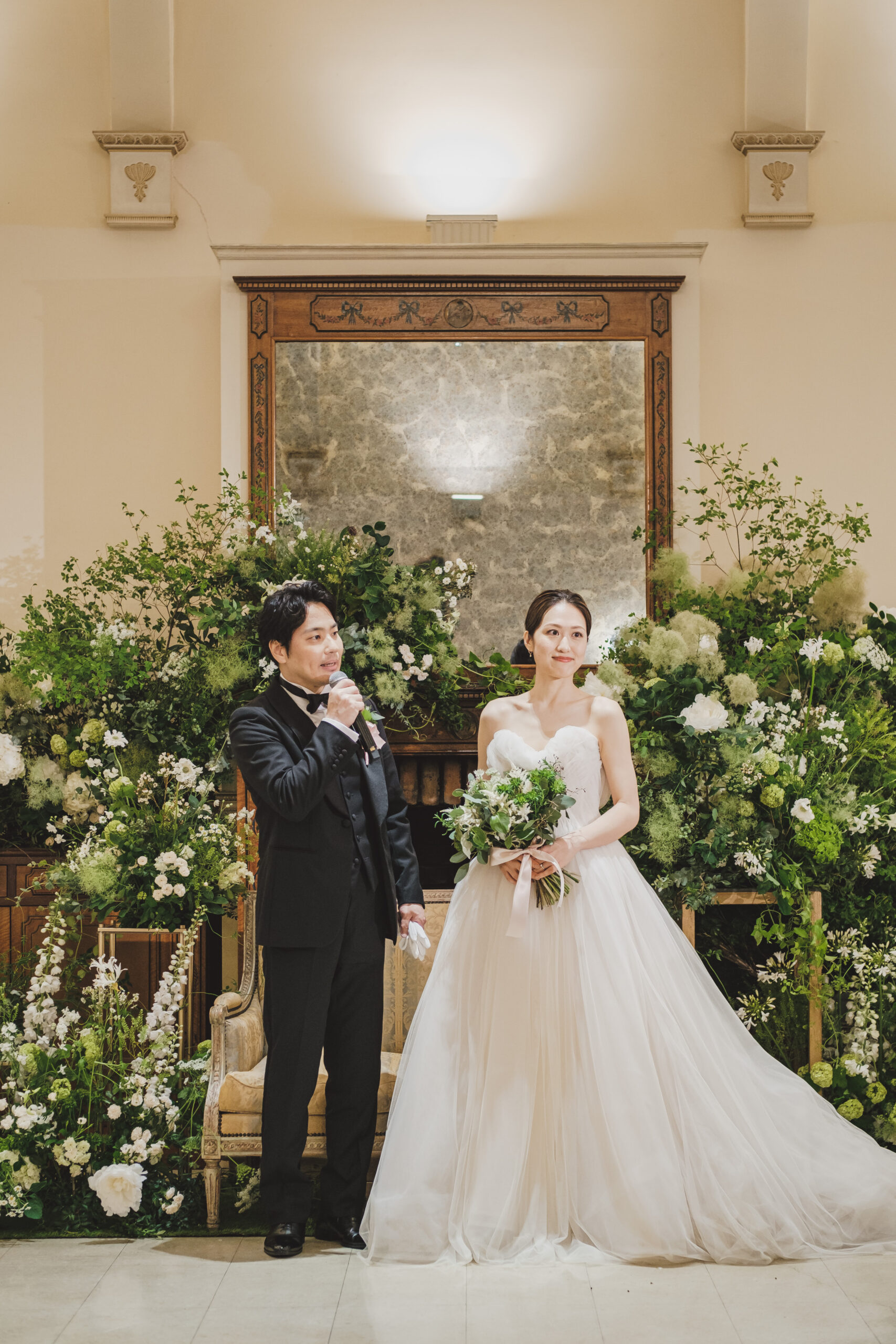 柔らかなブラッシュカラーのチュールをふんだんに使用したモニークルイリエのプリンセスラインのウェディングドレスをお色直しで纏うご新婦様とトリートジェントルマンのブラックのタキシードに身を包むご新郎様