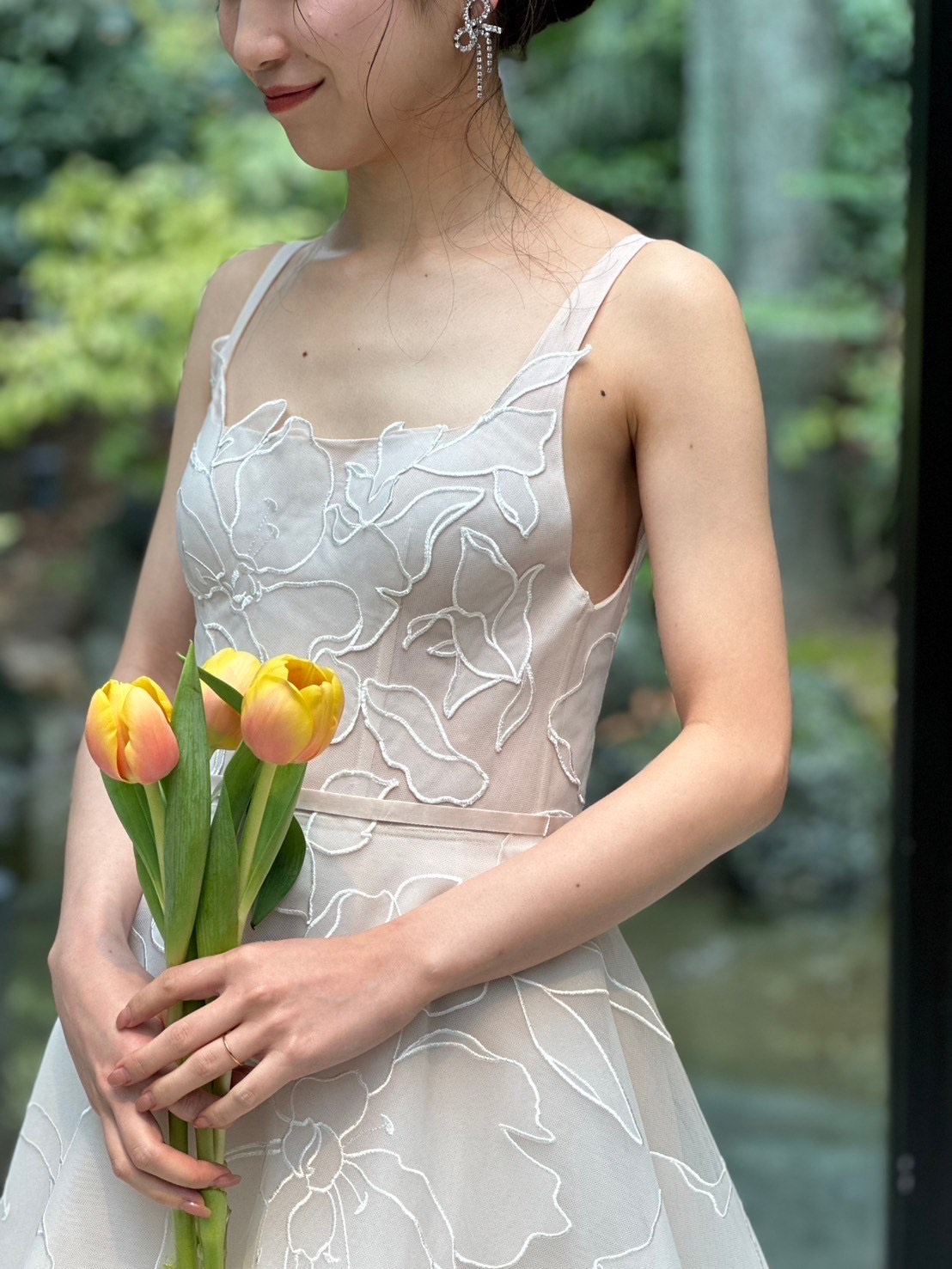 立体的なフラワーモチーフが施されたミラ ズウィリンガーのウェディングドレスには耳元に遊び心溢れるリボンモチーフを合わせて特別感のあるコーディネートにします