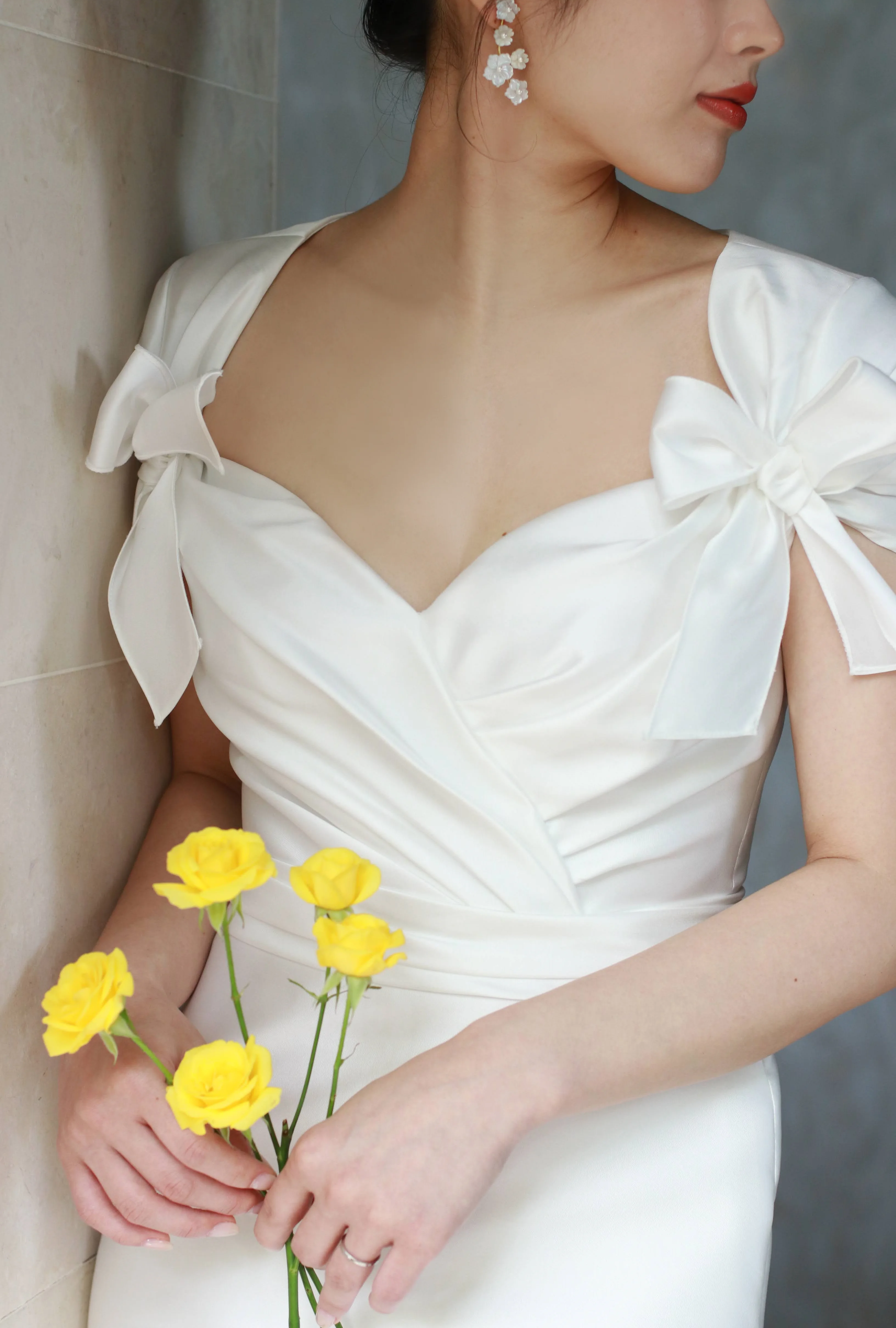 真っ白なシルクサテンが美しいインポートブランドのリーム アクラのウェディングドレスには、優しく華やかな黄色のブーケや、乳白色のジェニファー ベアのフラワーモチーフのイヤリングを合わせたロマンティックなコーディネートがおすすめ