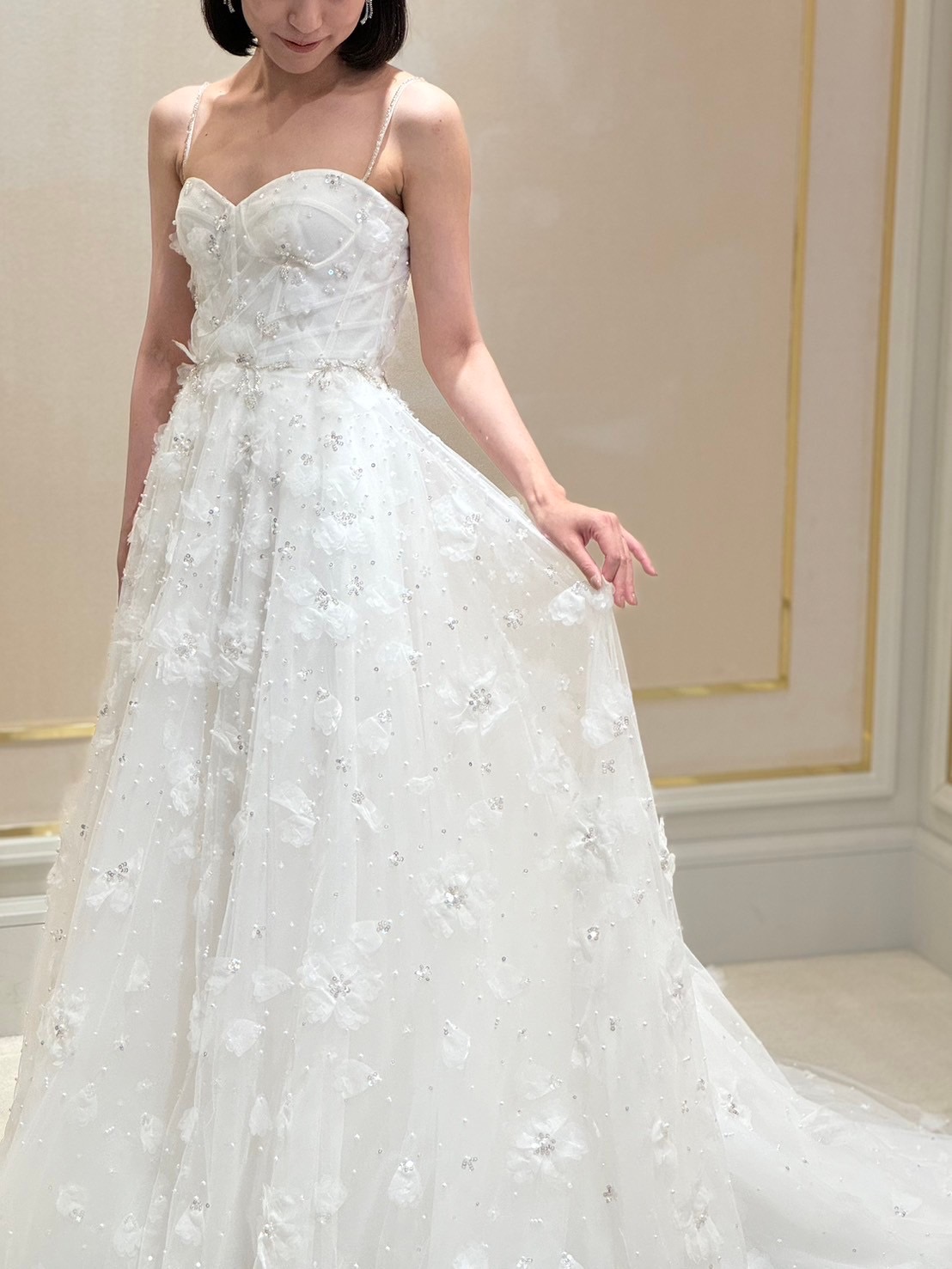 時代を超えて愛され続けるAラインの王道なシルエットに、細かなビジューと愛らしいフラワーモチーフが施されており花嫁を上品な輝きと可憐なオーラで包み込むウェディングドレス