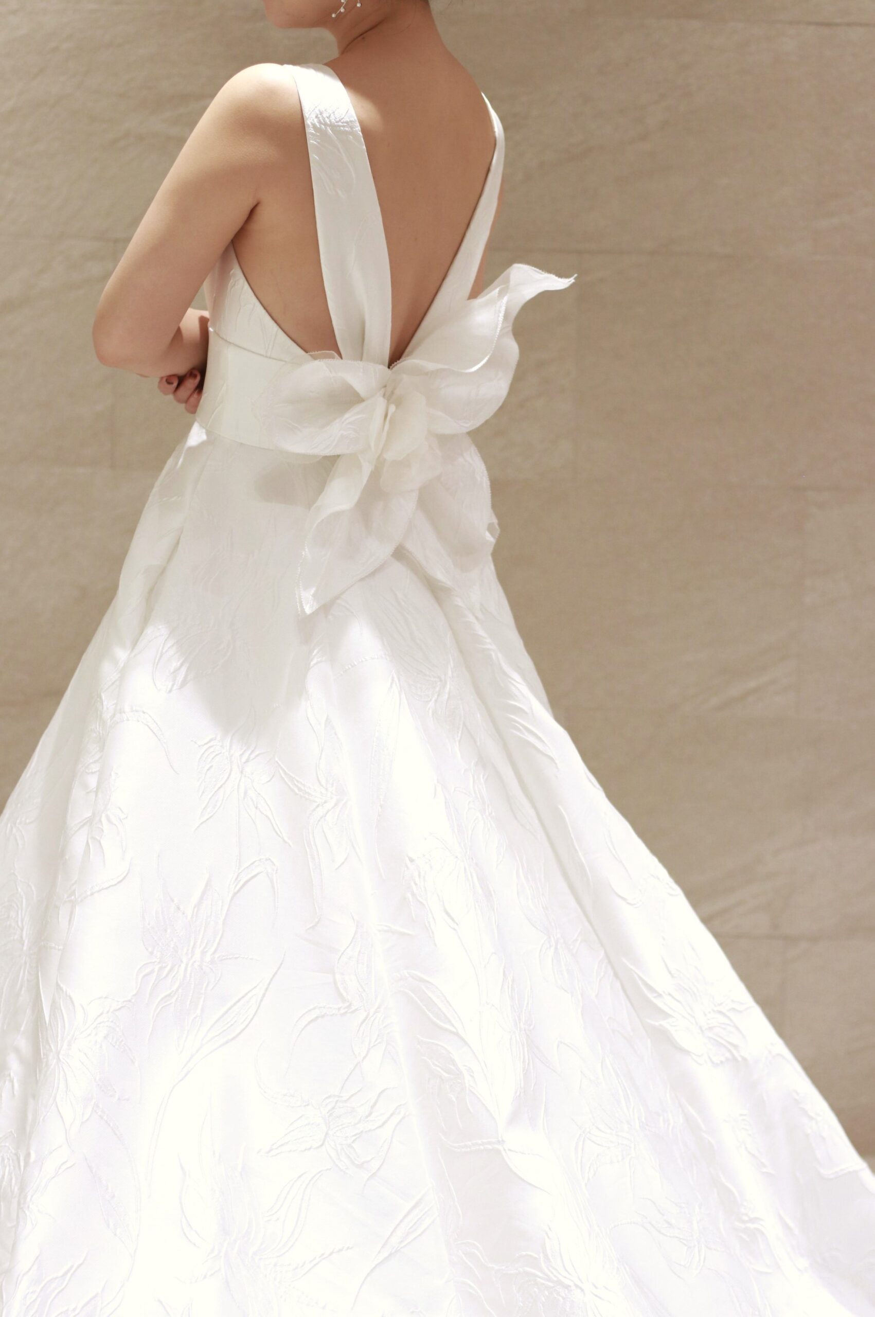 バックコンシャスなアムサーラのウェディングドレスは、可憐さを象徴するユリの花をかたどり上品さとエレガントさを引き立てる立体感のあるモチーフが印象的な一着です。