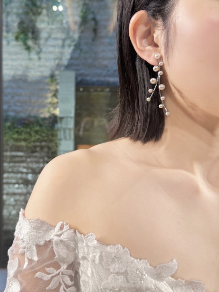 作り込み過ぎないタイトなヘアスタイルにデコルテラインをより綺麗に見せてくれるパールのロングイヤリングを添えることで、上品かつ可憐な印象にしてくれる新作ウェディングドレス。