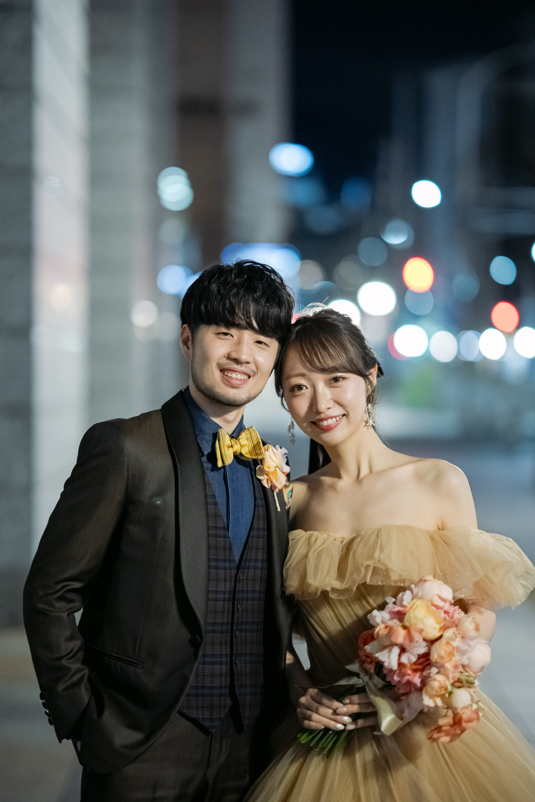 カルーゾのタキシードにセブンフォールドの蝶ネクタイ、ボリエッロのシャツを着た新郎と、トリートメゾンのベージュゴールドのカラードレスを着た花嫁