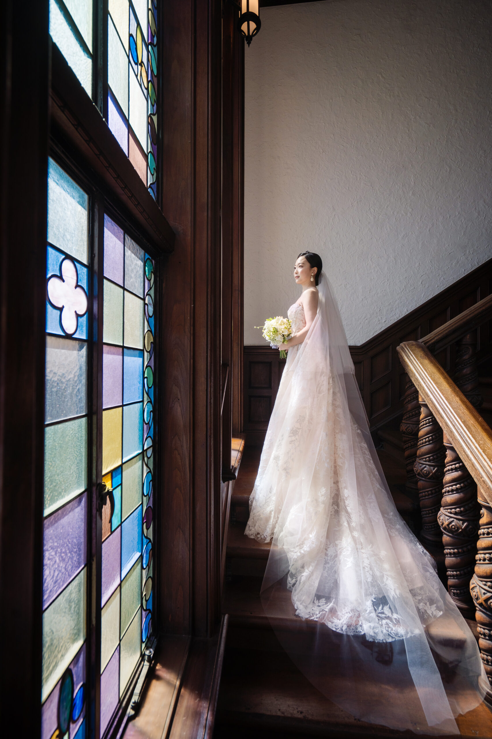 赤坂プリンスクラシックハウスのフォトスポットであるステンドグラスの前で、光を集めるご新婦様が纏うのは、モニークルイリエの刺繍とスパンコールが美しいAラインのウェディングドレスです。